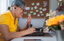 Uma mulher usando fones de ouvido sorri e acena para algu&eacute;m em uma reuni&atilde;o virtual.
