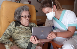Um profissional da sa&uacute;de usando m&aacute;scara olha para um tablet com um paciente.