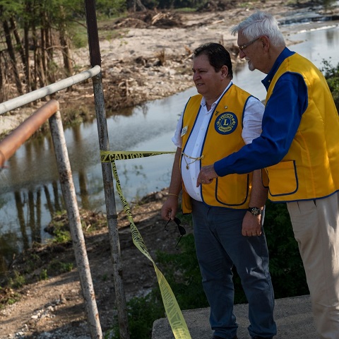 O presidente do Conselho de LCIF, Fabrício Oliveira, e um Leão local na margem de um rio atingido pelas cheias.