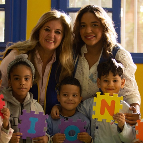 Dois adultos e três crianças sorrindo e segurando peças de quebra-cabeça com letras.